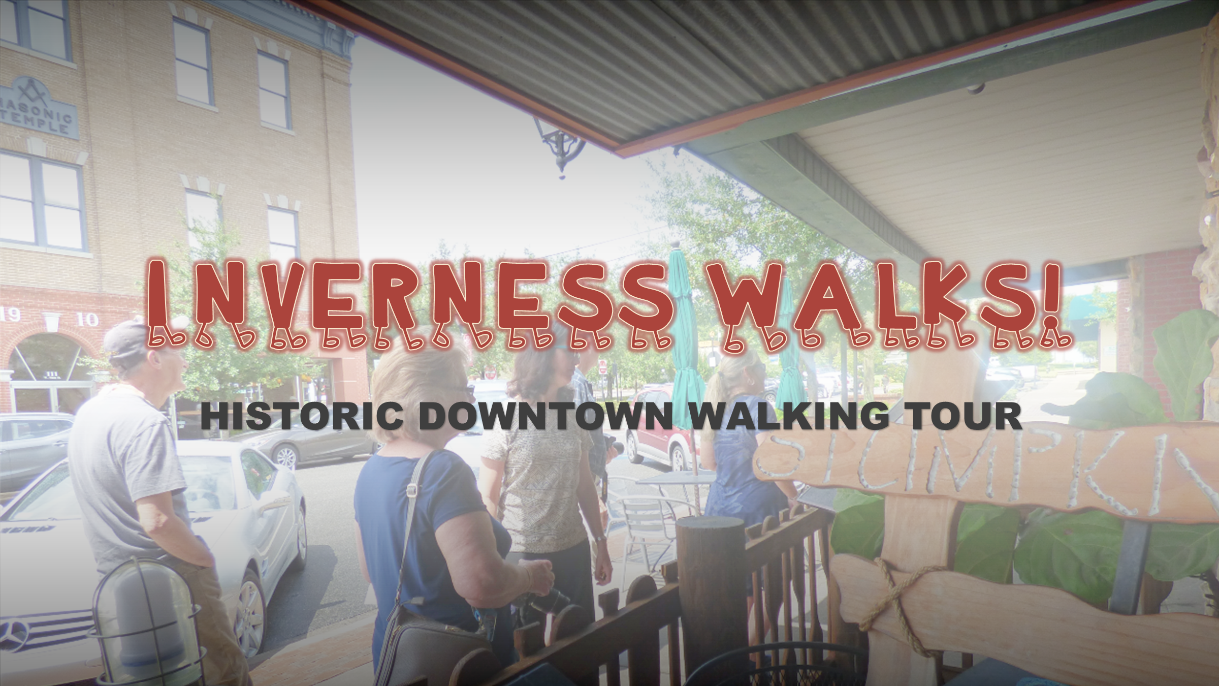 Group of people walking on a downtown street, with the 1910 Historic Masonic Building in the background. Inverness Walks: Historic Downtown Walking Tour is overlaid on the image.